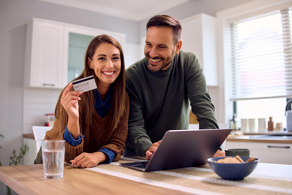 Payment Plans. A couple smiling holding a credit card in front of a laptop.