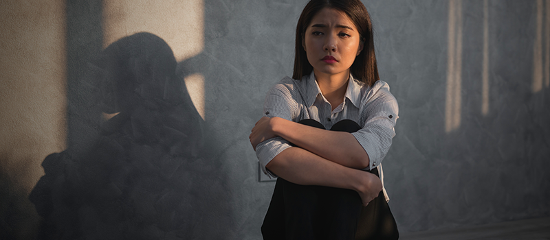 Visa Psychological Evaluations. A woman with her arms crossed sitting on the floor that has been crying.